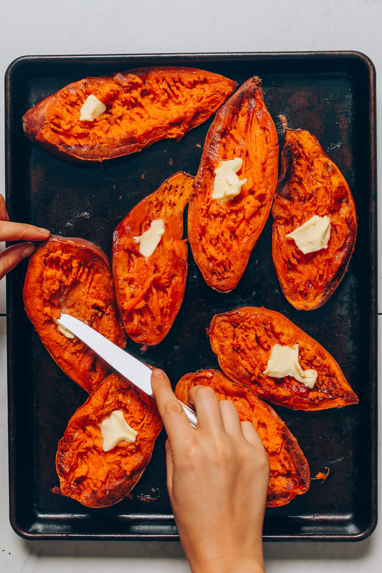 Using a knife to spread vegan butter onto halved Sweet Potato Boats