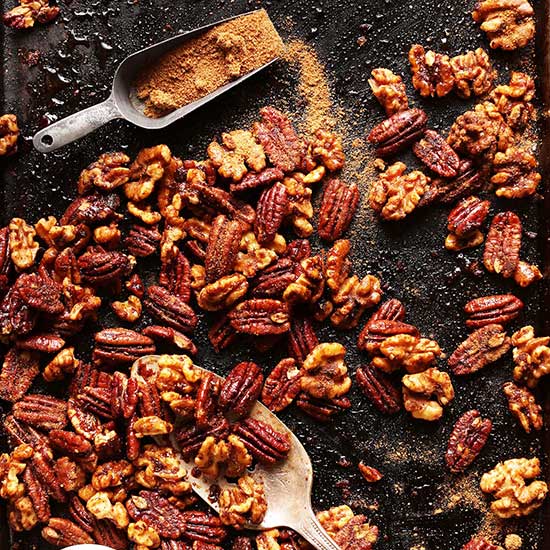 Baking sheet with a scoop of coconut sugar and batch of Candied Spiced Nuts