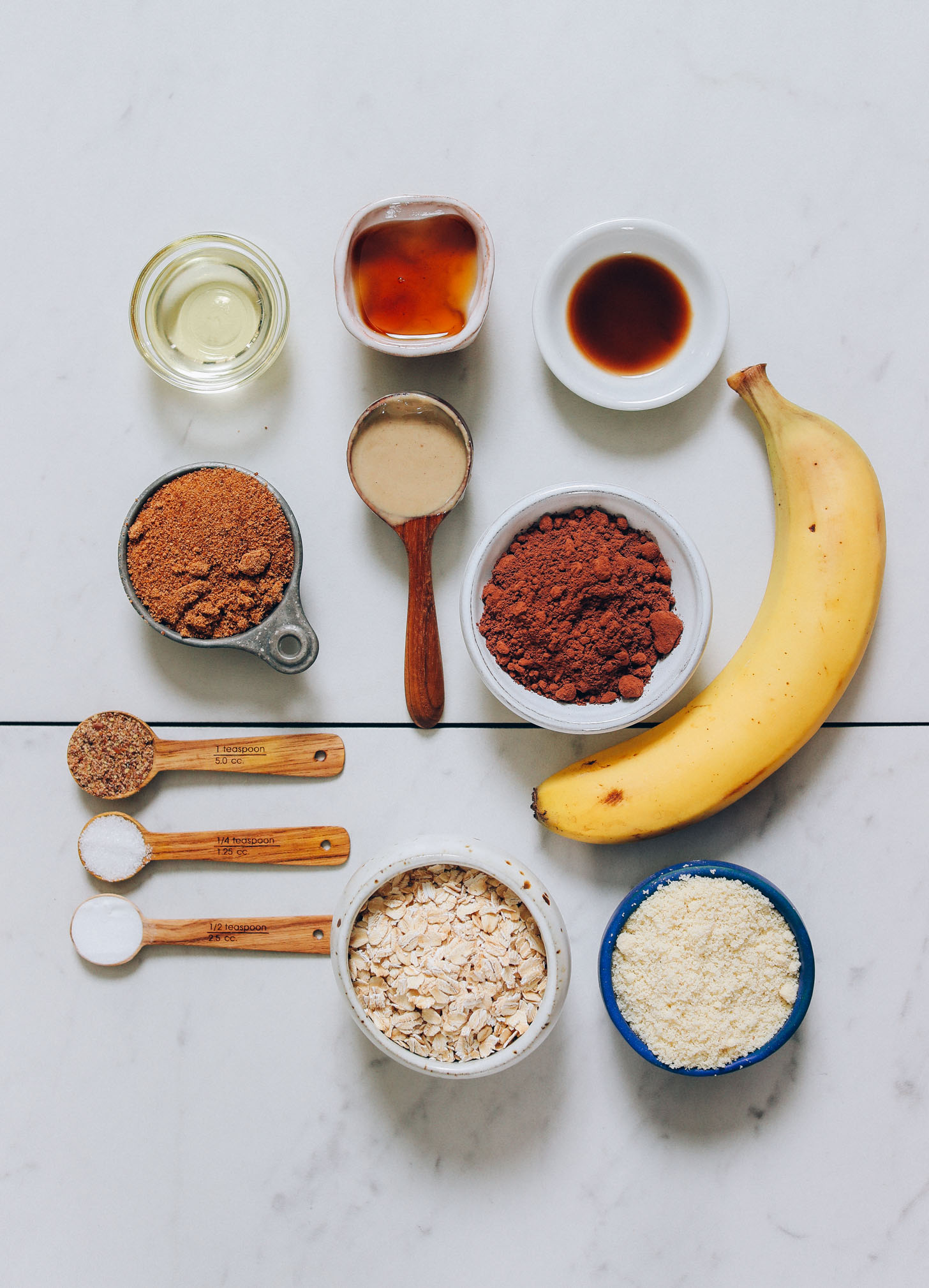 Banana, almond flour, oats, cocoa powder, coconut sugar, maple syrup, and other ingredients for making Banana Chocolate Muffins